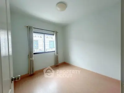 Bright empty bedroom with wooden flooring and large window, perfect for customization.