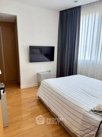 Modern bedroom with sleek TV and elegant curtains, featuring a cozy bed and wooden flooring.
