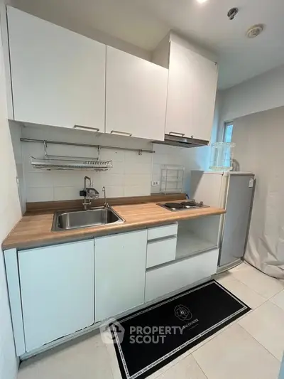 Modern compact kitchen with sleek white cabinets and wood countertop, featuring a small fridge and electric stove.