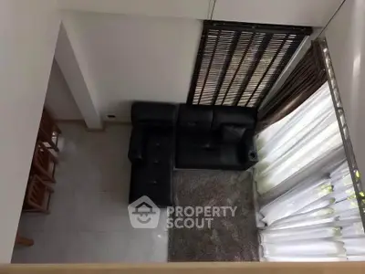 Modern living room with black leather sofa and large window curtains, offering a cozy and stylish ambiance.