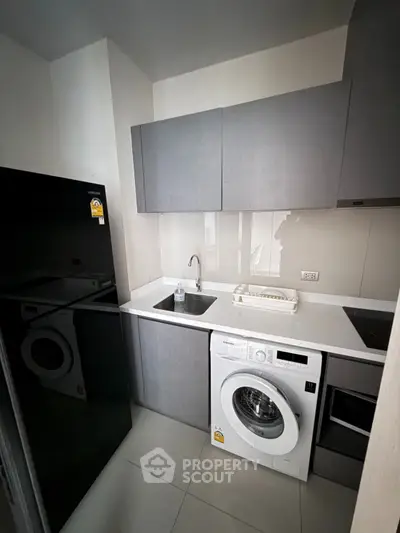 Modern kitchen with sleek cabinets, washing machine, and black fridge in compact layout.