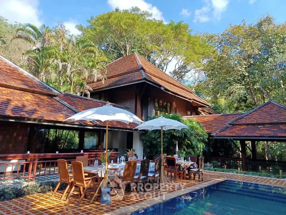 Luxurious tropical villa with pool and outdoor dining area surrounded by lush greenery.