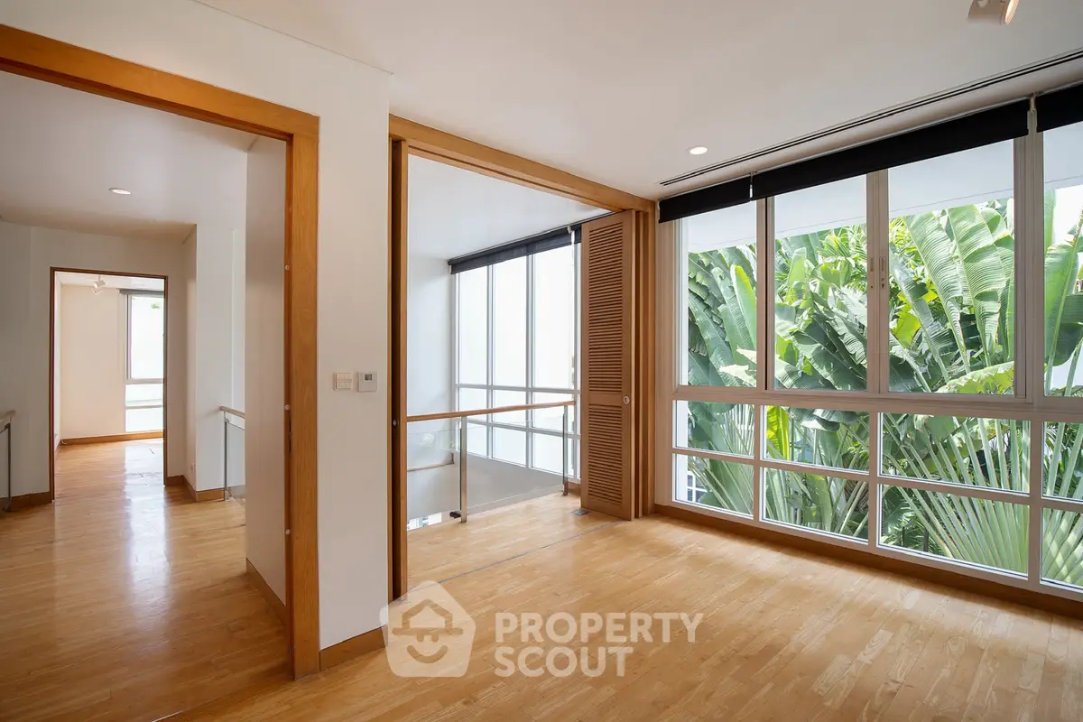 Spacious modern hallway with large windows and wooden flooring, offering a serene view of lush greenery.