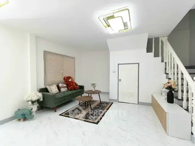 Modern living room with stylish decor and staircase, featuring a plush sofa and elegant lighting.