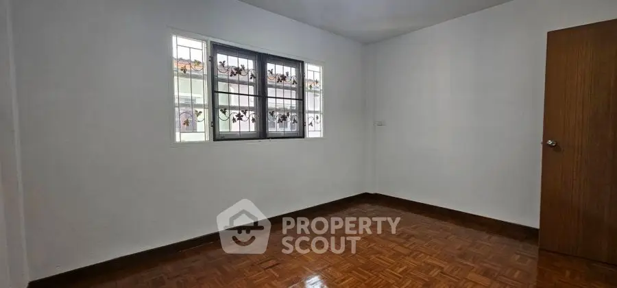 Spacious empty room with wooden flooring and decorative window grills.