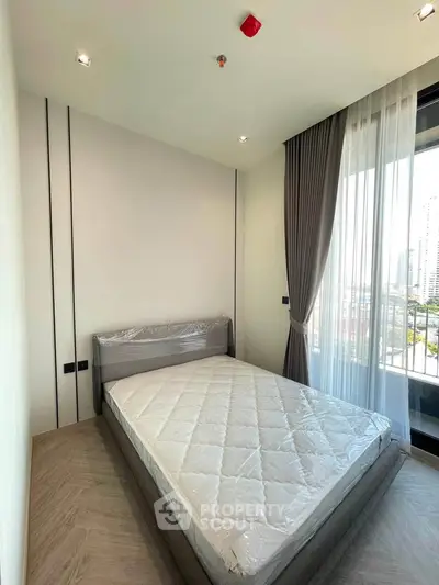 Modern bedroom with large window and city view, featuring a neatly made bed and elegant curtains.