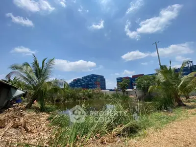 Scenic view of modern buildings with lush greenery and a serene pond under a clear blue sky.