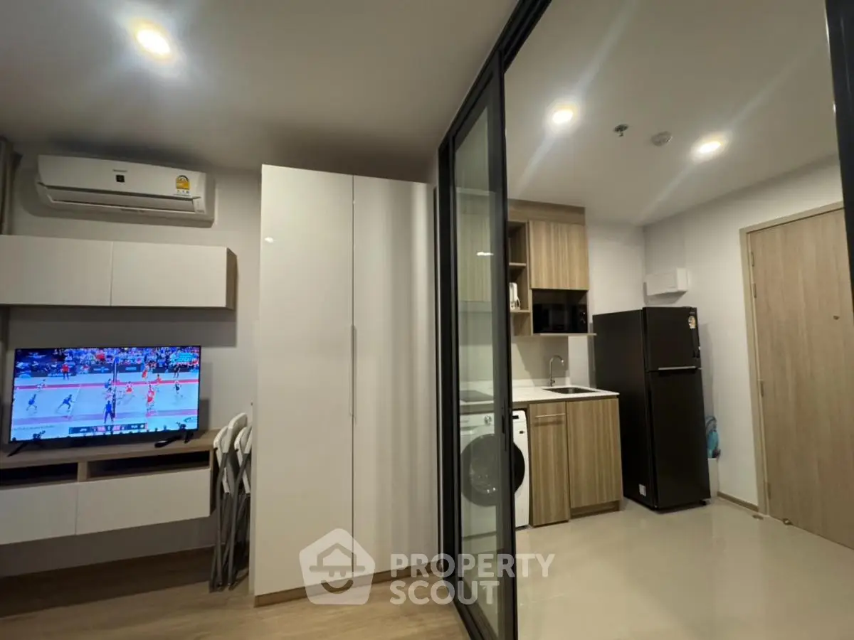 Modern apartment interior with sleek kitchen and cozy living area featuring a TV and air conditioning.