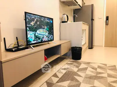 Modern living room with sleek TV setup and compact kitchen area in open layout apartment.