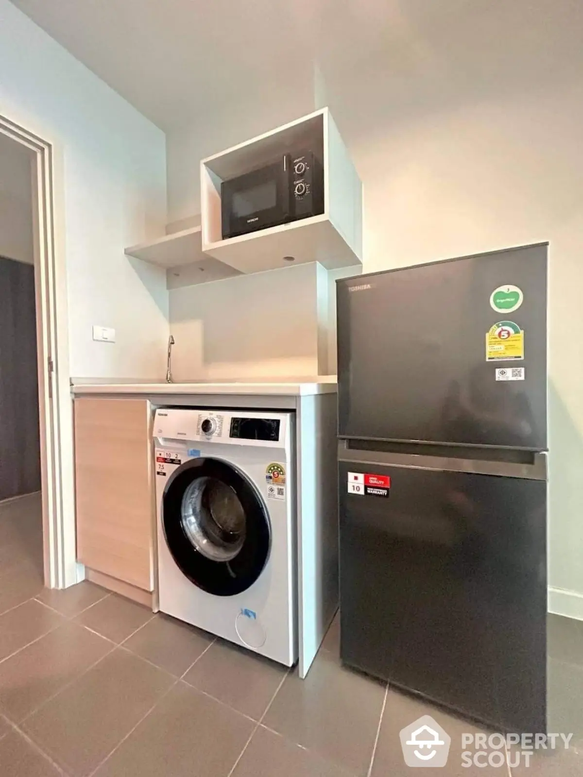 Modern kitchen with washing machine, fridge, and microwave in compact layout.