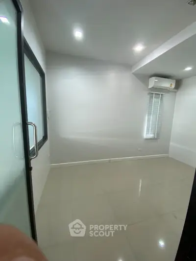 Spacious empty room with air conditioning and glass door, ideal for office or study setup.