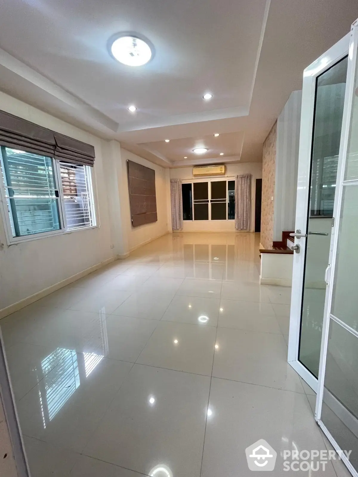 Spacious and bright living room with glossy tiled flooring, recessed lighting, and large windows inviting ample natural light, perfect for modern living.