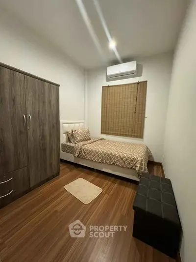 Cozy bedroom with wooden flooring, modern wardrobe, and air conditioning unit.