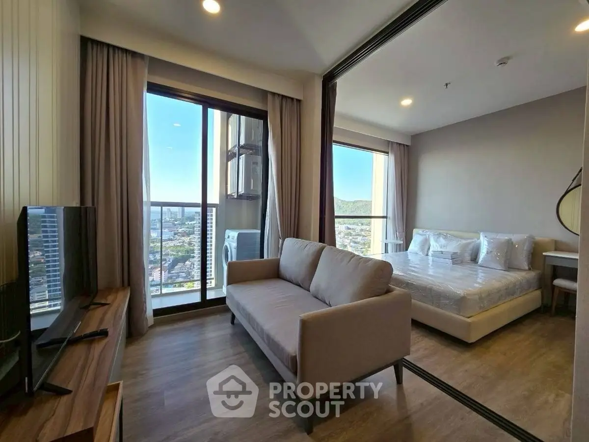 Modern condo with open living room and bedroom, featuring large windows and city view.