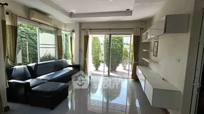 Spacious modern living room with large windows and garden view, featuring sleek furniture and abundant natural light.