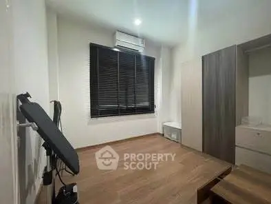 Spacious bedroom with modern furnishings and wooden flooring, featuring a large window with blinds.