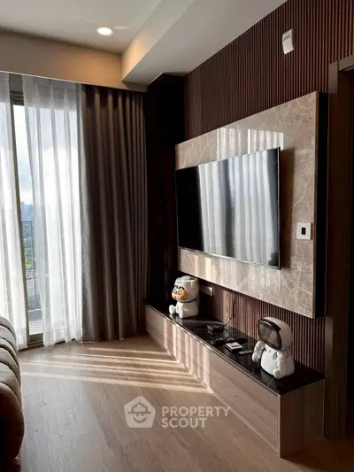 Modern living room with large TV, stylish decor, and floor-to-ceiling windows offering natural light.