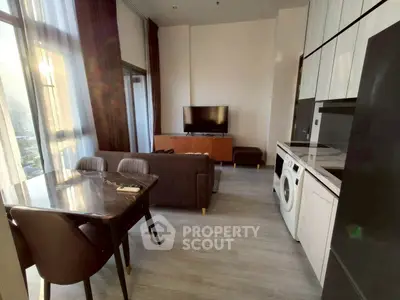Modern living room with open kitchen and washing machine, featuring sleek furniture and abundant natural light.