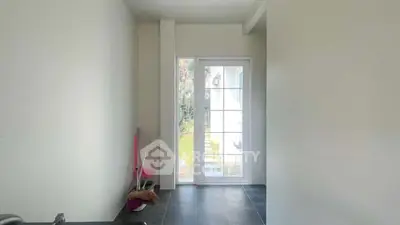 Bright interior space with glass door leading to garden, featuring tiled flooring and minimal decor.
