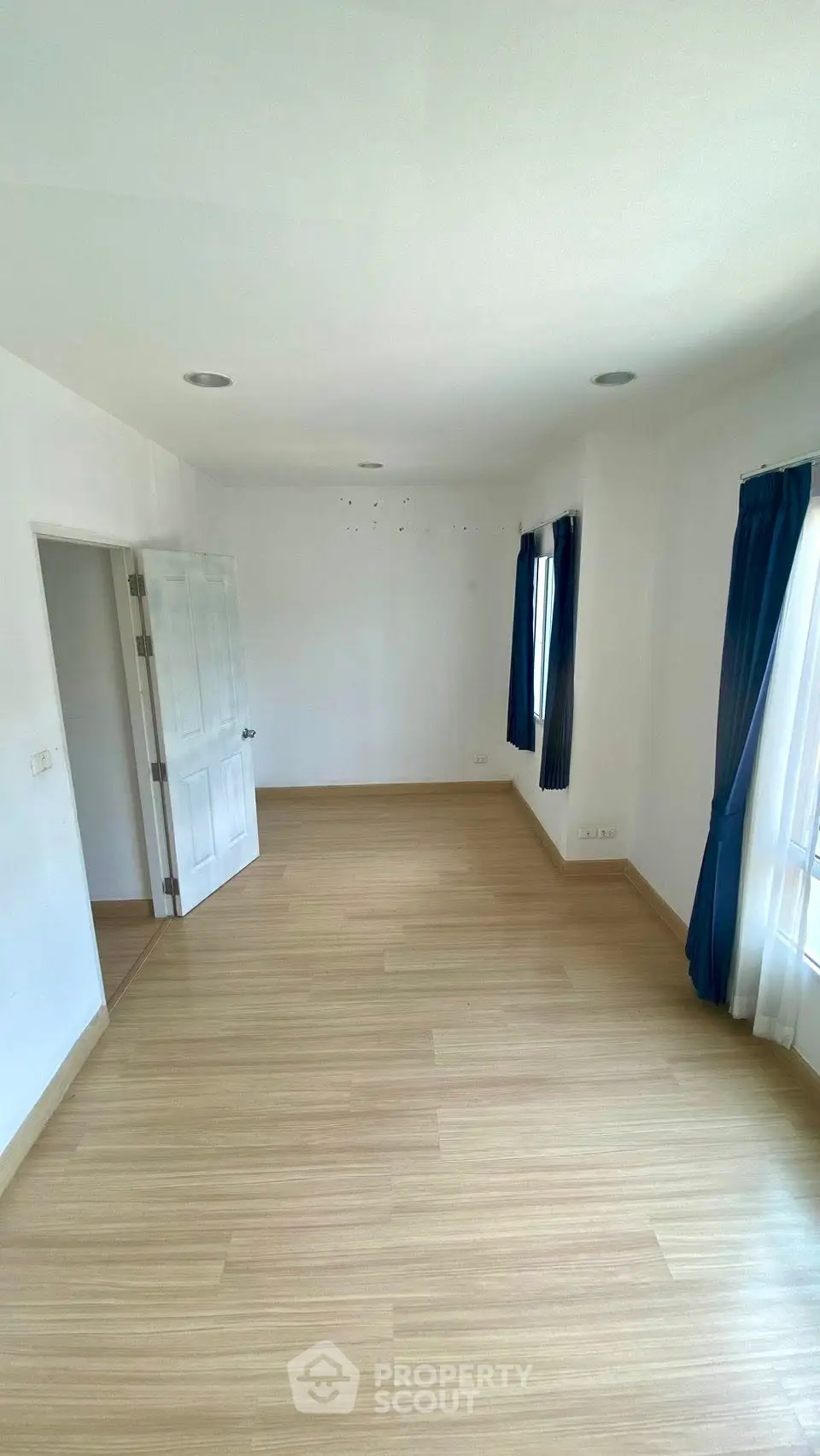 Spacious empty room with wooden flooring and blue curtains, perfect for customization.