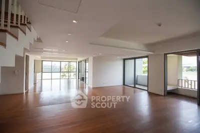 Spacious open-plan living room with large windows and balcony access, featuring elegant wooden flooring.
