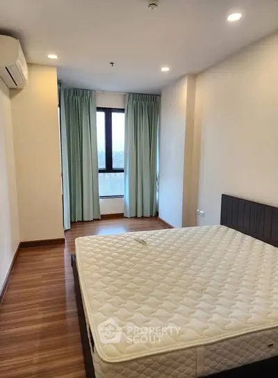 Spacious bedroom with large window and modern furnishings in a well-lit apartment.