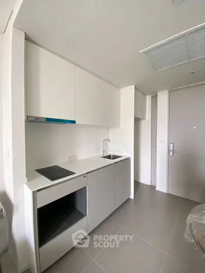 Modern minimalist kitchen with sleek white cabinetry and induction cooktop.