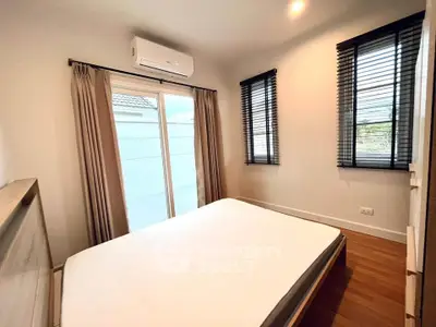 Cozy bedroom with natural light and modern design, featuring large windows and air conditioning.