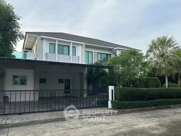 Spacious modern two-story house with lush greenery and gated driveway.