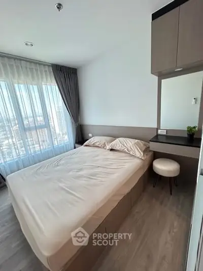 Cozy bedroom with large window and modern furnishings in a high-rise apartment.