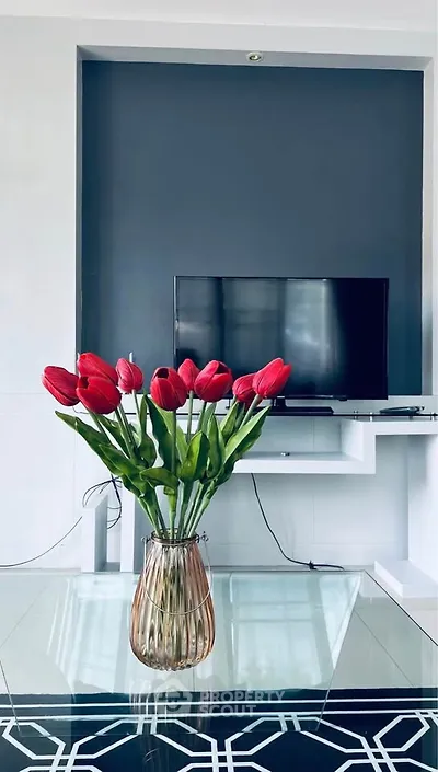 Modern living room with stylish TV setup and elegant vase of red tulips.