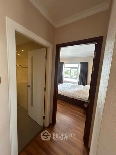 Cozy apartment hallway leading to a bright bedroom with wooden flooring and large window.