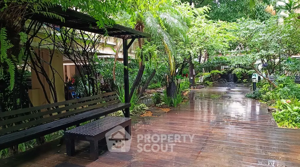 Lush garden pathway with wooden deck and seating area in serene residential complex.
