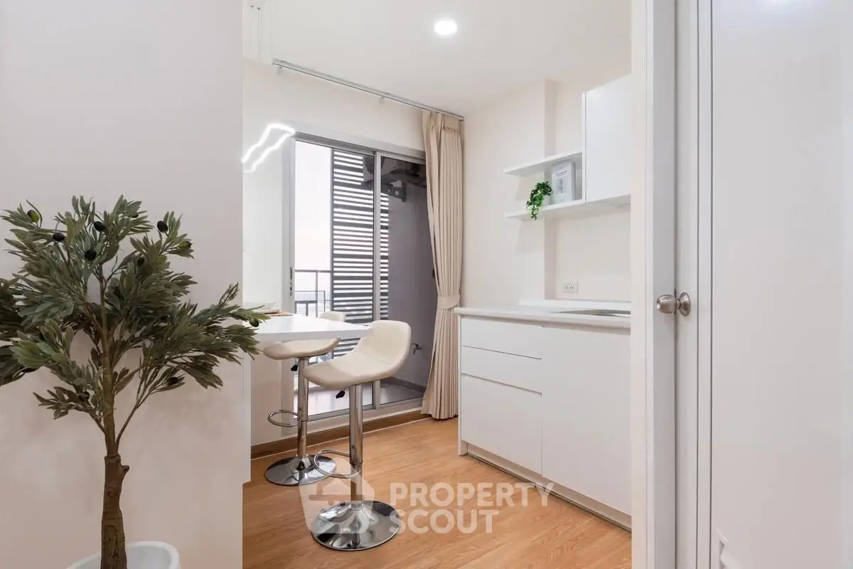 Modern kitchen with open layout and balcony access, featuring sleek white cabinets and stylish bar stools.