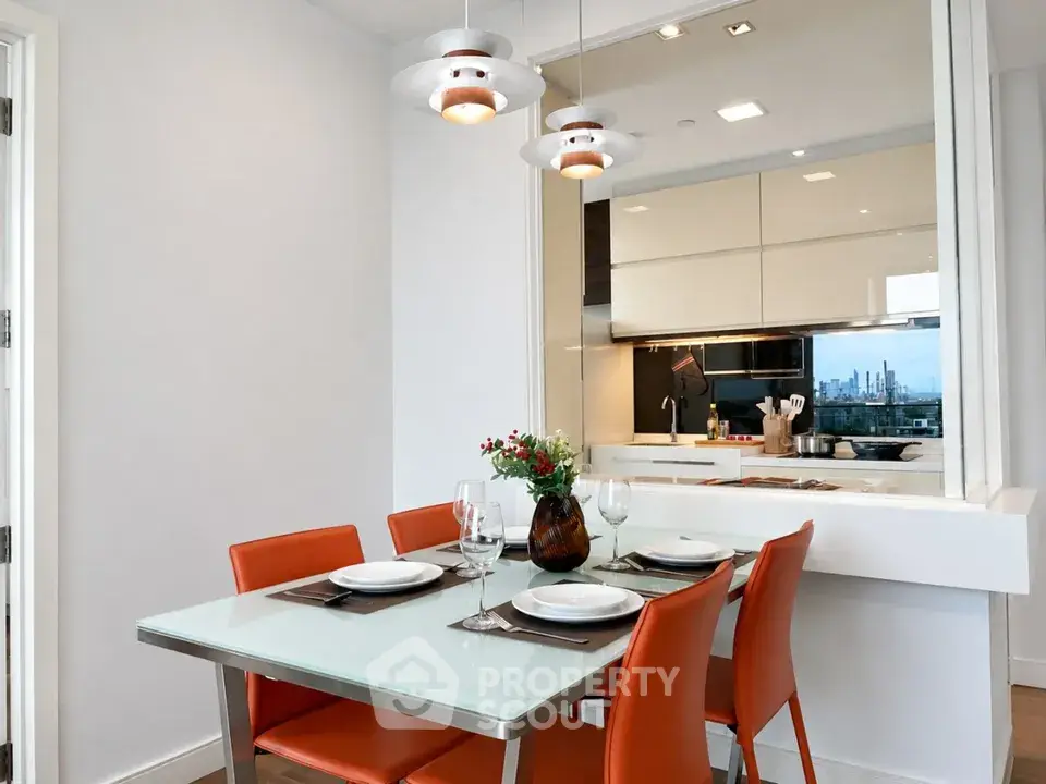 Modern dining area with glass table and orange chairs, open kitchen layout, city view.
