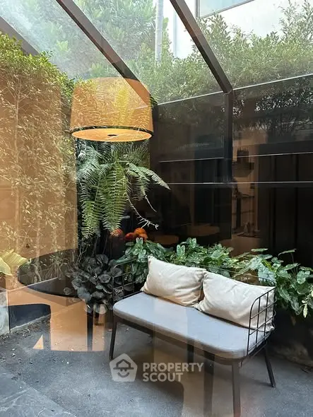 Charming garden patio with cozy seating and lush greenery under a glass roof.