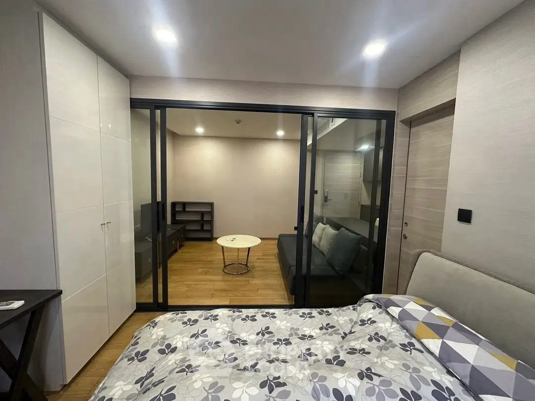 Modern bedroom with glass partition and cozy living area, featuring stylish decor and ample lighting.