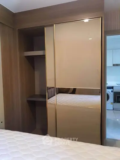 Modern bedroom with sleek built-in wardrobe and glimpse of kitchen appliances.