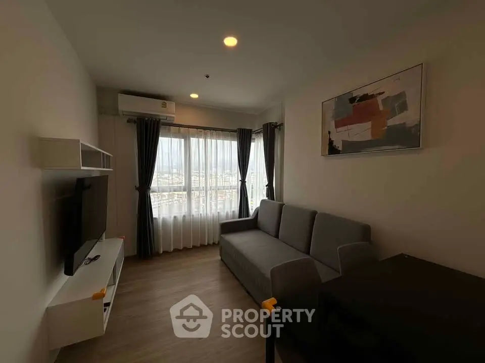 Modern living room with sleek furniture and large window offering city views.