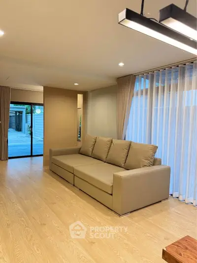 Modern living room with beige sofa and large windows, featuring elegant lighting and wooden flooring.
