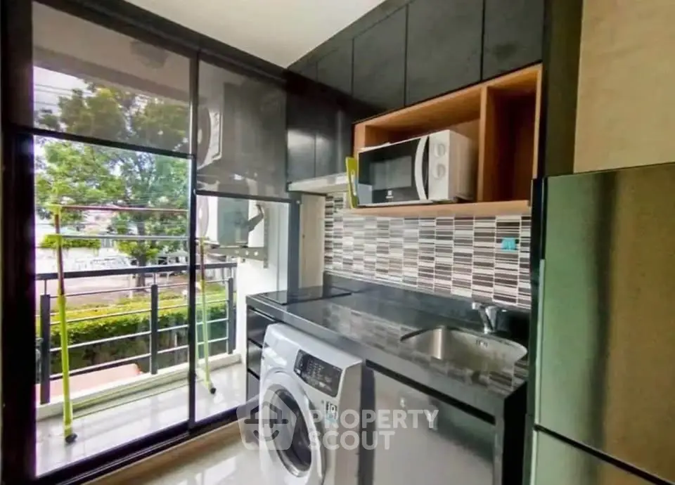 Modern kitchen with washing machine, microwave, and sleek cabinetry overlooking a lush garden view.