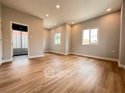 Spacious empty room with wooden flooring and large windows, perfect for customization.