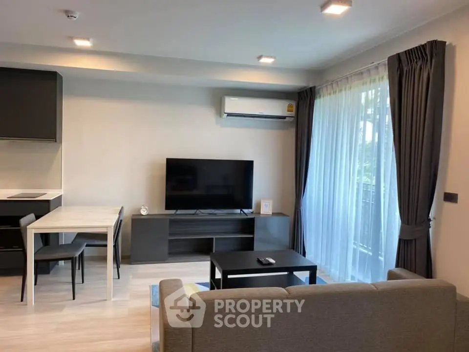 Modern living room with sleek furniture and large TV, featuring natural light from floor-to-ceiling windows.