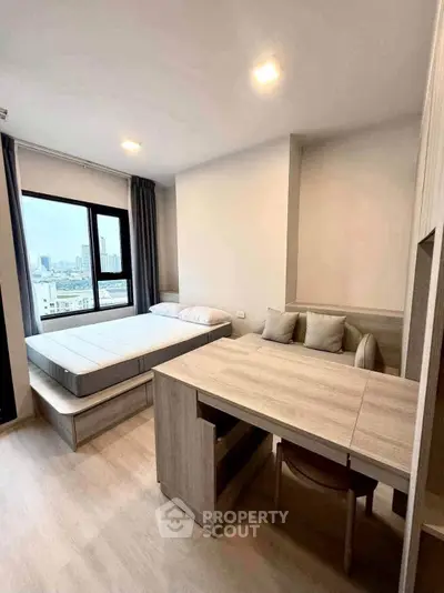 Modern studio apartment with bed and dining area, featuring large window with city view.