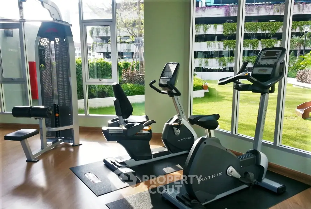 Modern gym with exercise equipment and garden view in luxury apartment complex.