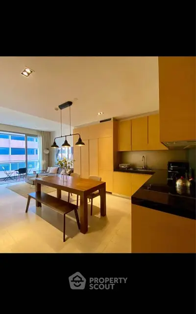 Modern open-layout kitchen and dining area with sleek wooden cabinetry and stylish lighting.