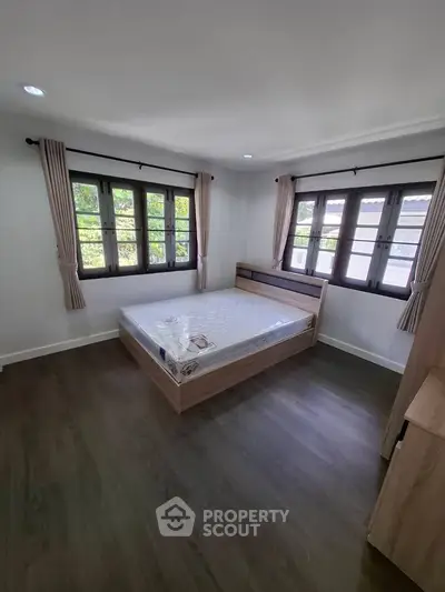 Spacious bedroom with large windows and wooden flooring, offering natural light and a cozy atmosphere.