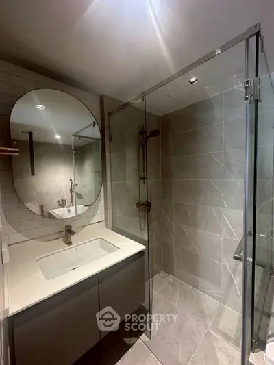 Modern bathroom with glass shower and sleek vanity in contemporary apartment.