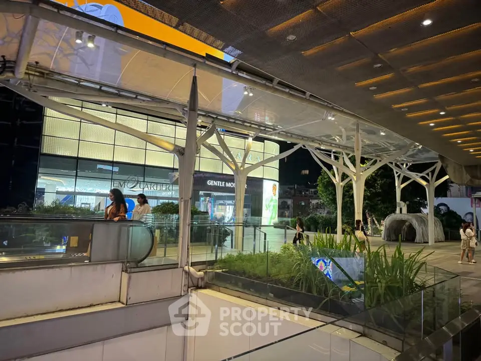 Modern shopping mall entrance with escalators and greenery at night