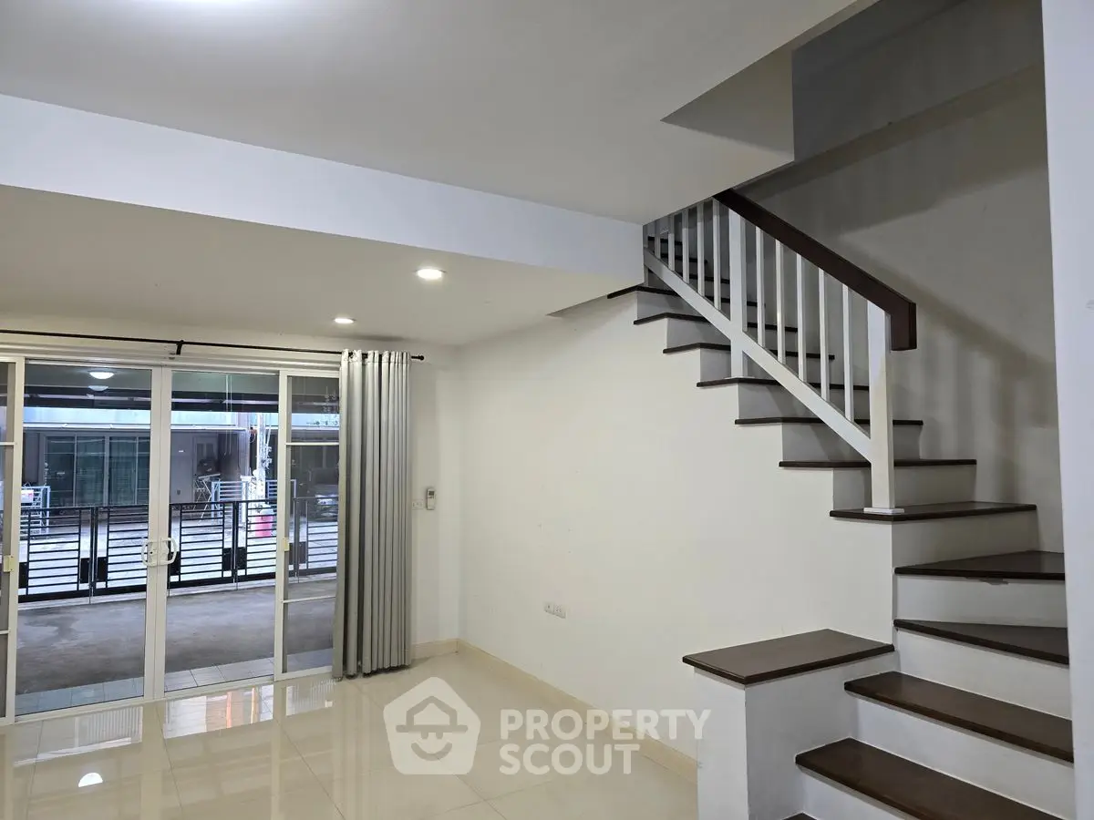 Spacious modern living room with sleek staircase and large windows for natural light.